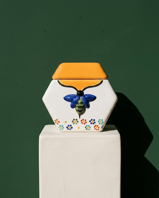 De Todas Las Flores on a bone-white plinth against a deep green wall. Hand-painted ceramic from Santa María Canchesdá holding raw wildflower honey.